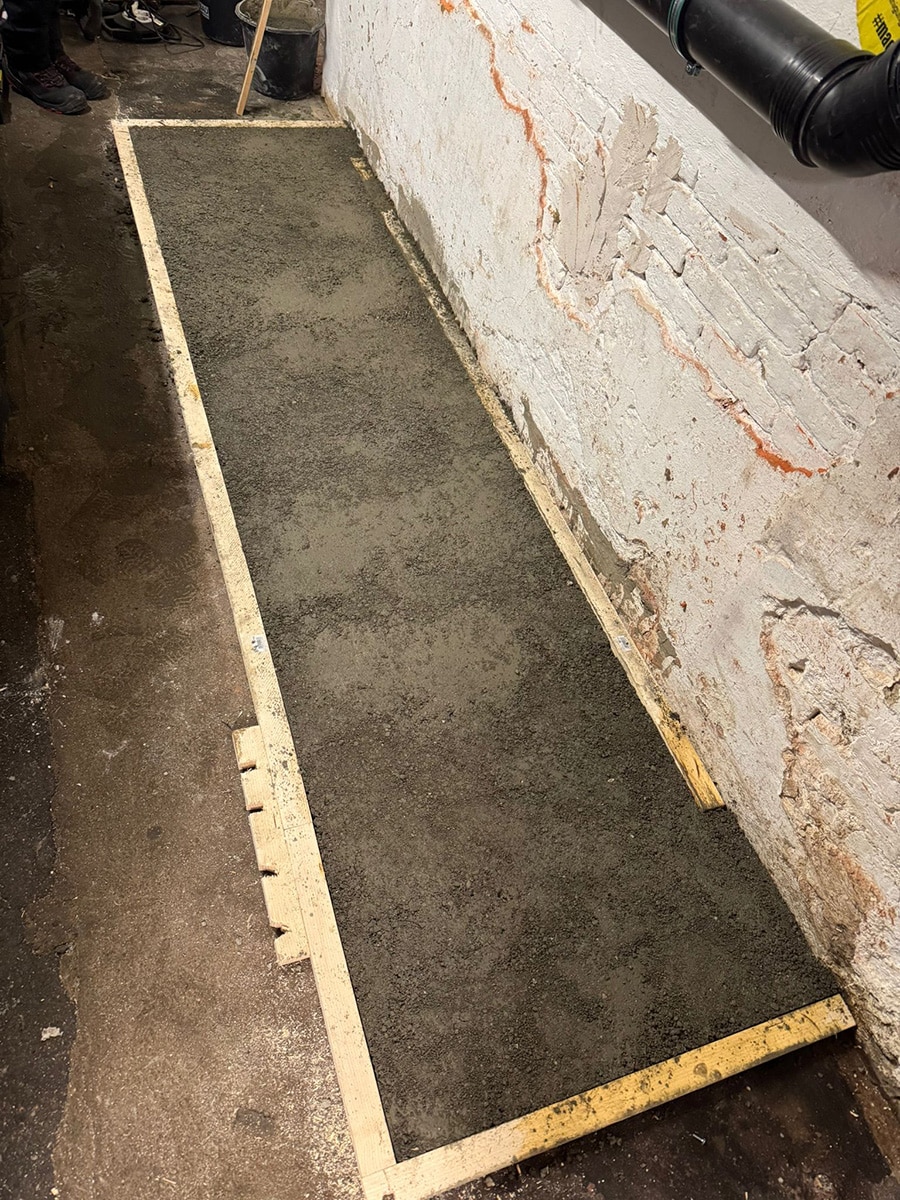 Frisch betonierte rechteckige Aufstellfläche mit Holzschalung entlang einer Kellerwand