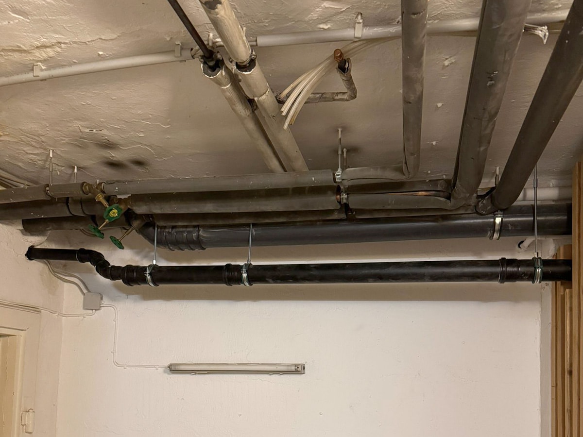 Mehrere schwarze Rohrleitungen parallel unter einer Kellerdecke
